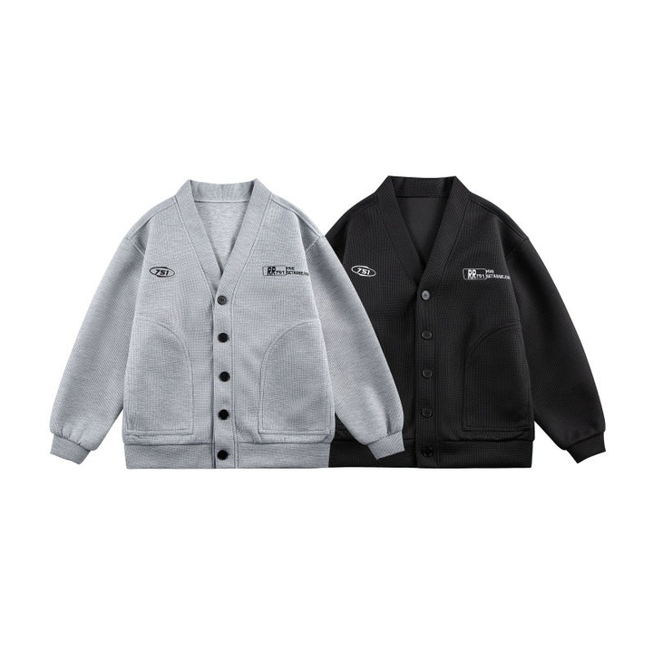 Unisex Boxy-Strickjacke im Waffelstrick mit V-Kragen, durchgehender Knopfleiste und aufgesetzten Rundtaschen Drune