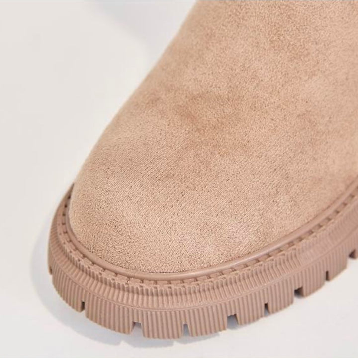 Detailansicht der Spitze eines beigen Stiefeletten, die seine weiche Textur und robuste Sohle vor einem sauberen Hintergrund hervorhebt.